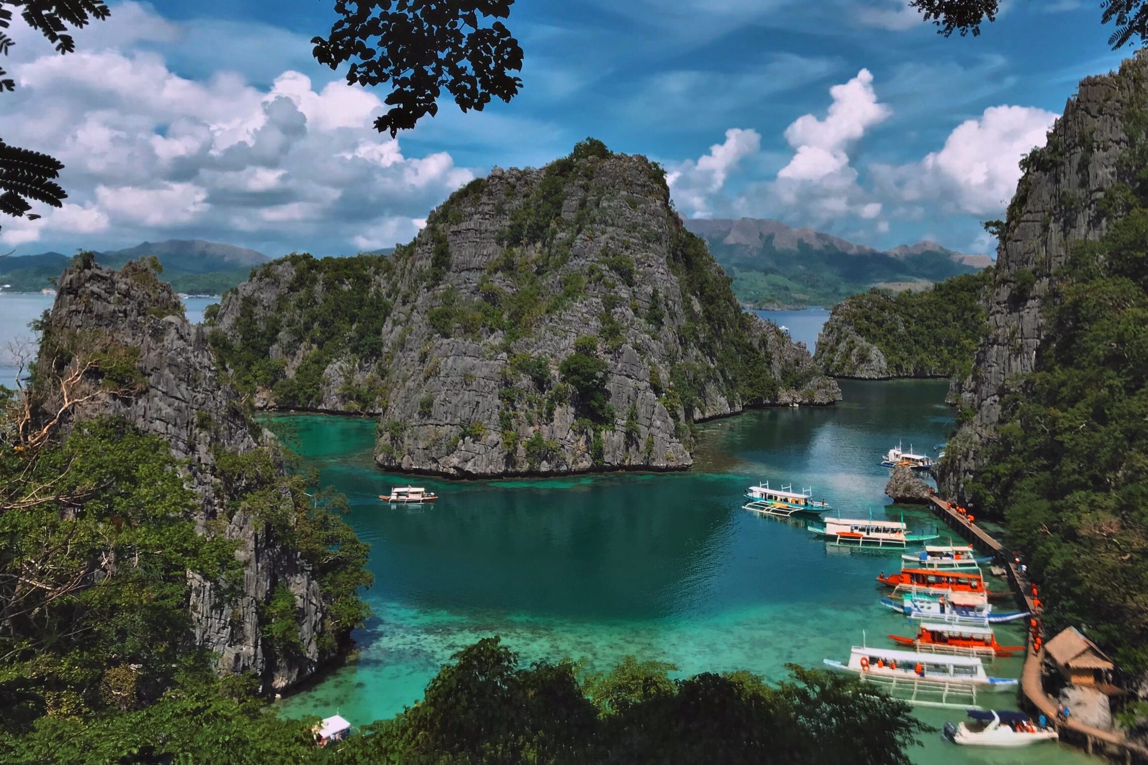 Aerial view of wooden boats docked in blue lagoon surrounded by limestone karsts