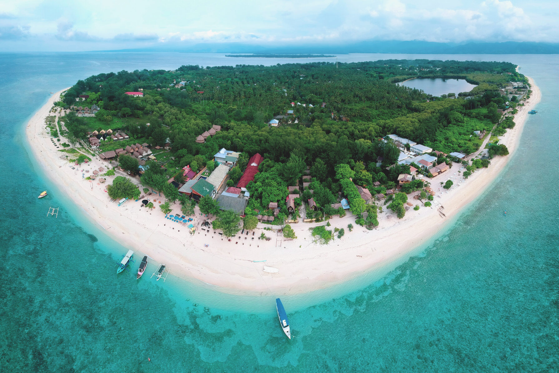 Aerial view of small island with green trees and white sand beach surrounded by a turquoise blue sea