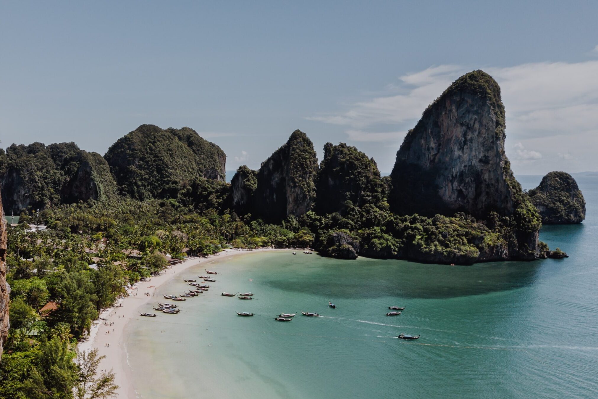 White sand beach with turquoise waters, green trees and tall limestone peaks