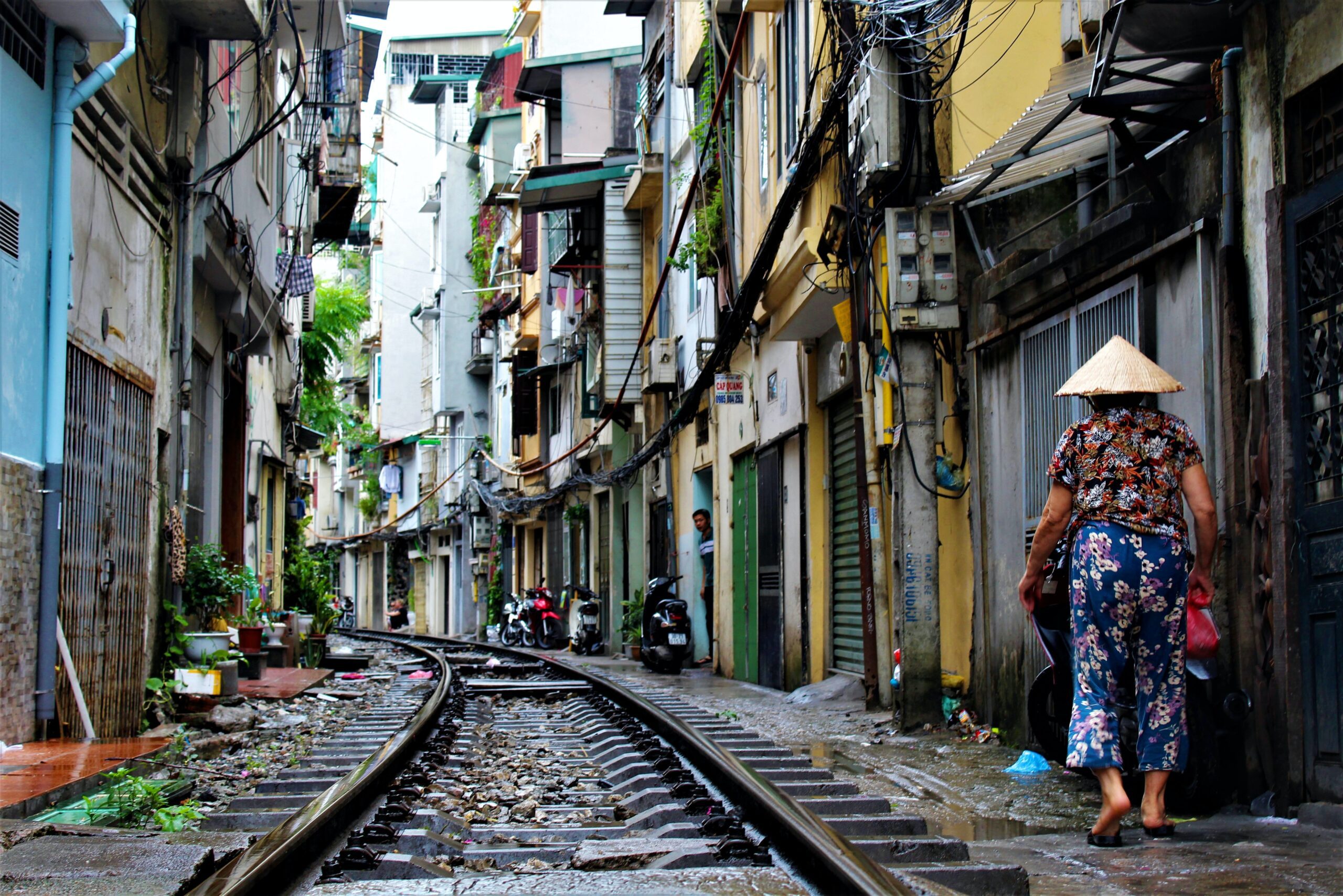 Vietnamese woman with traditional attire walking next to the railway on a narrow street