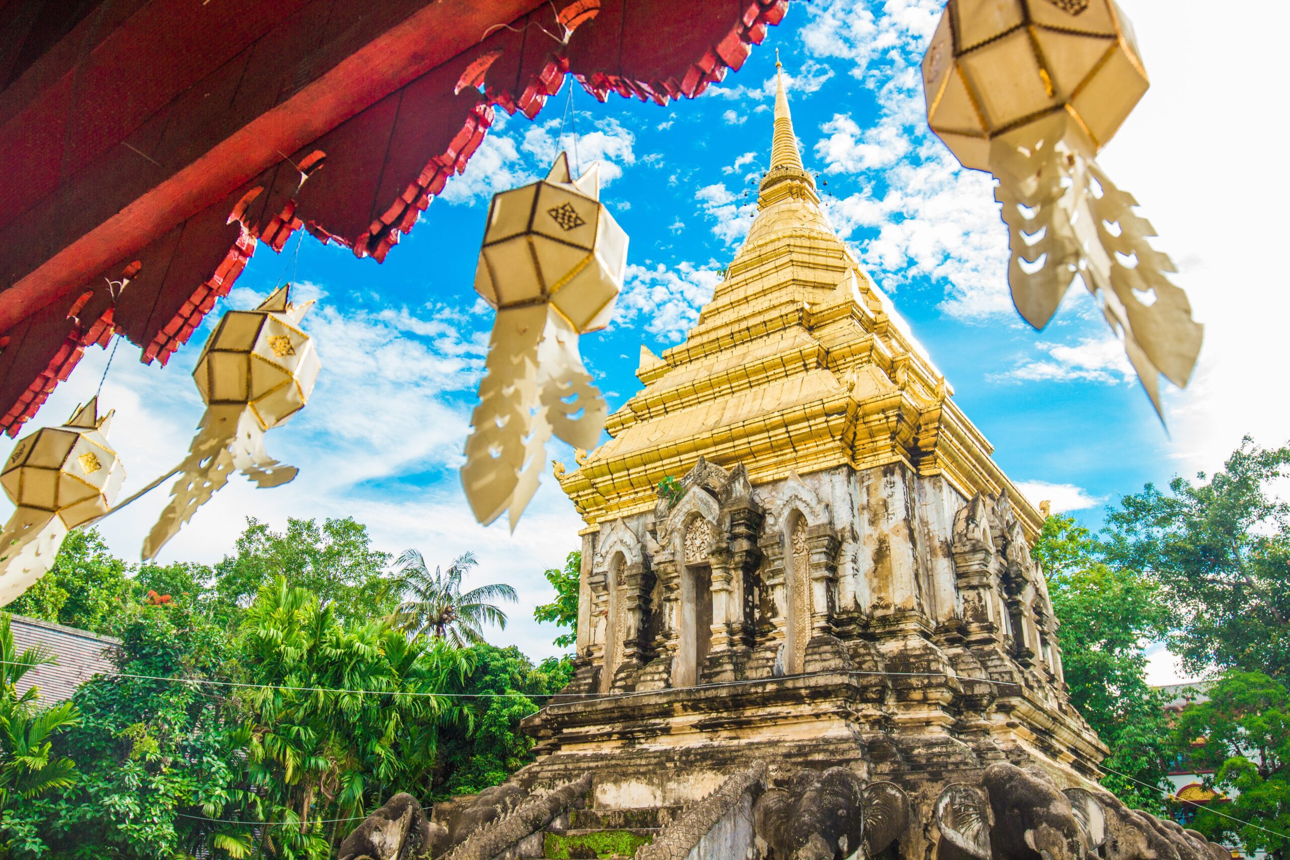 Ancient Thai Buddhist temple with golden roof and lanterns surrounded by greenery