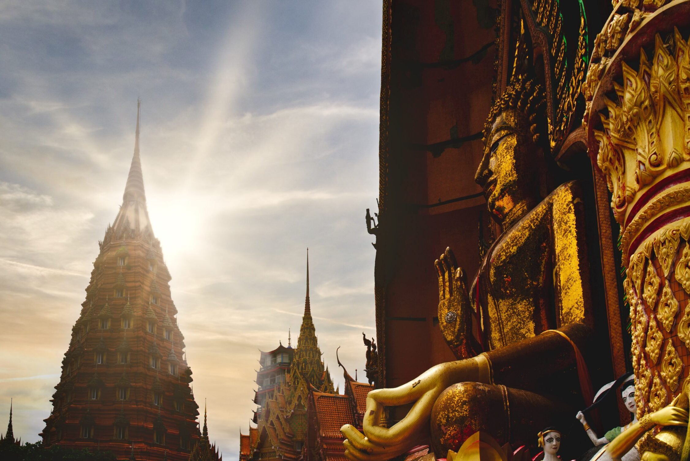 Thai Buddhist temple stupa and golden Buddha statue in front of the sun