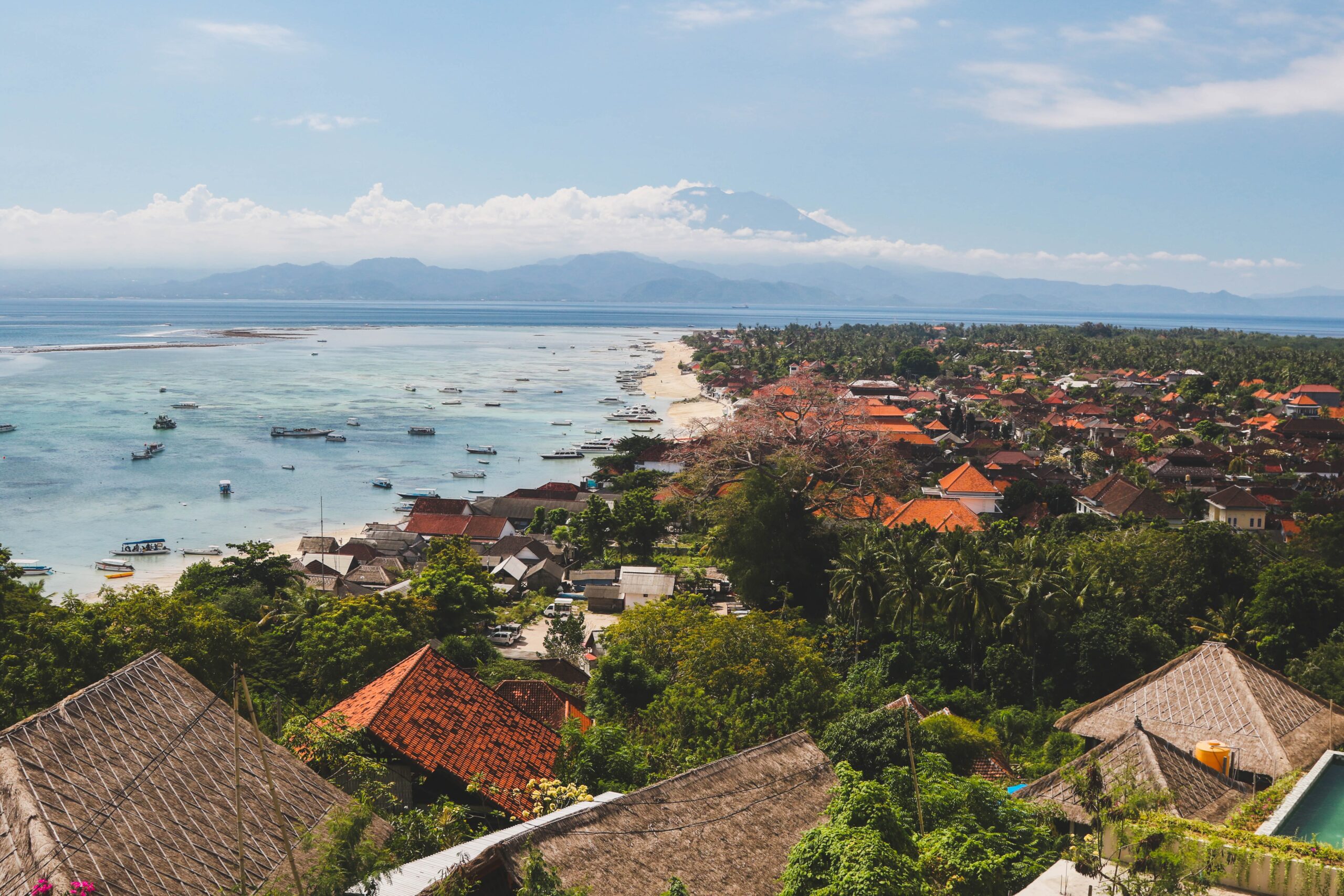 Hilltop view of seaside town roofs with boats and volcano during day time