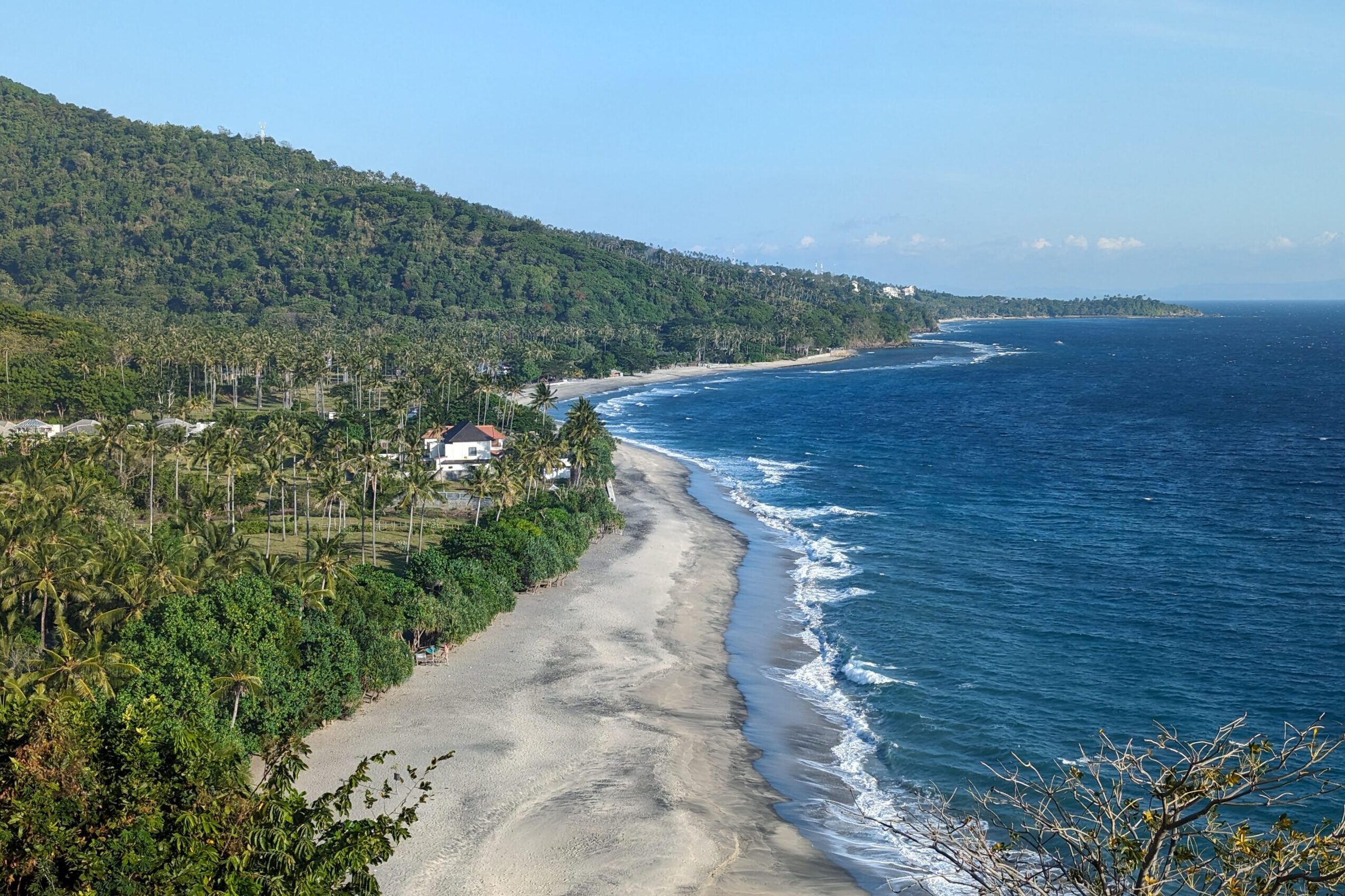 Panoramic view of a beach next to a lush hilll